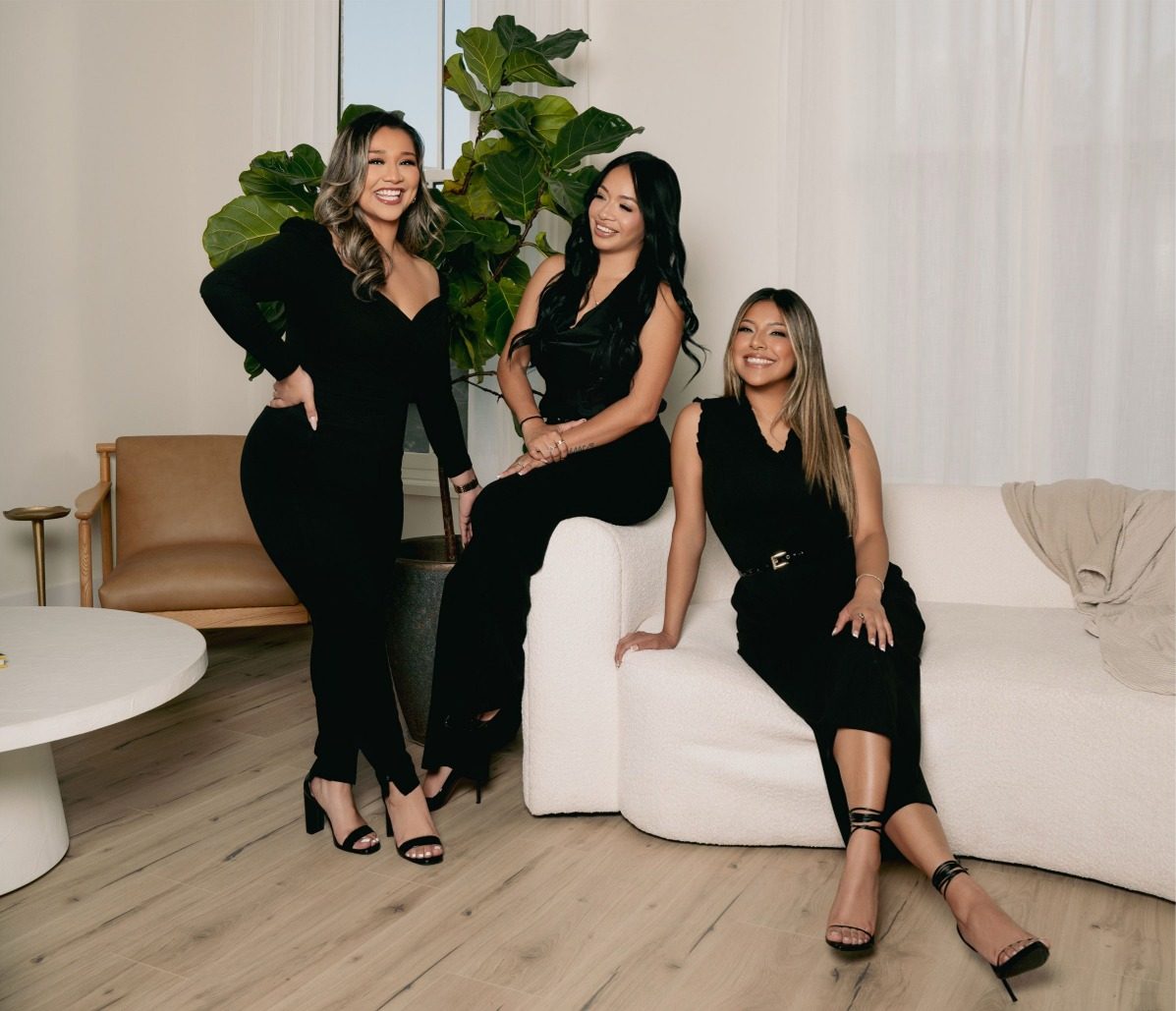 Three women tax preparers in black outfits pose together in a stylish, light-filled office.